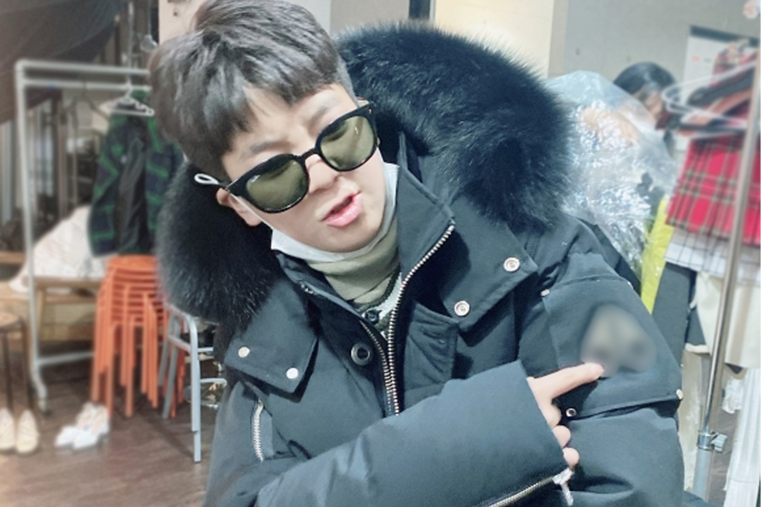 鄭東元在户外，雙手提起白色羽絨外套，背景是沙灘的場地