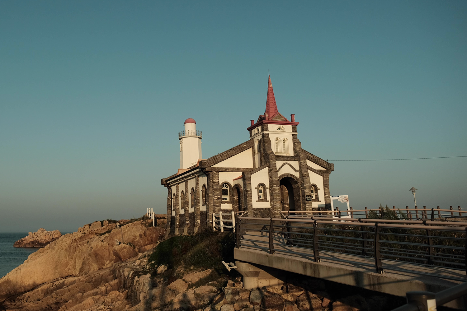 竹城聖堂坐落在海邊的風景，遠處的燈塔與碧藍的海水交相輝映。