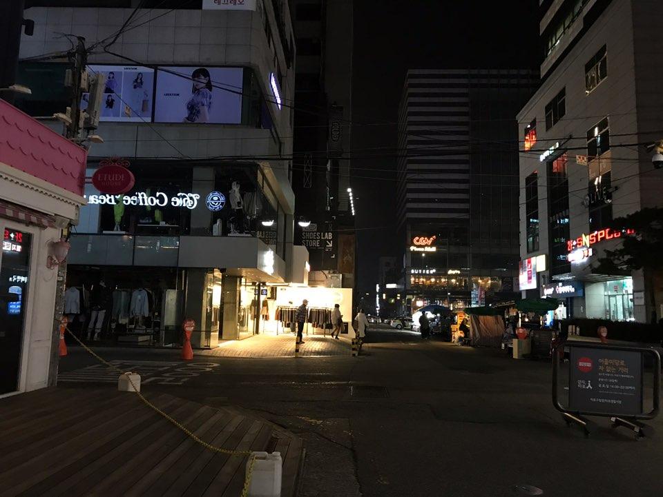 首尔弘大商店夜景，迎面是稀疏的路人，店外灯牌亮眼。