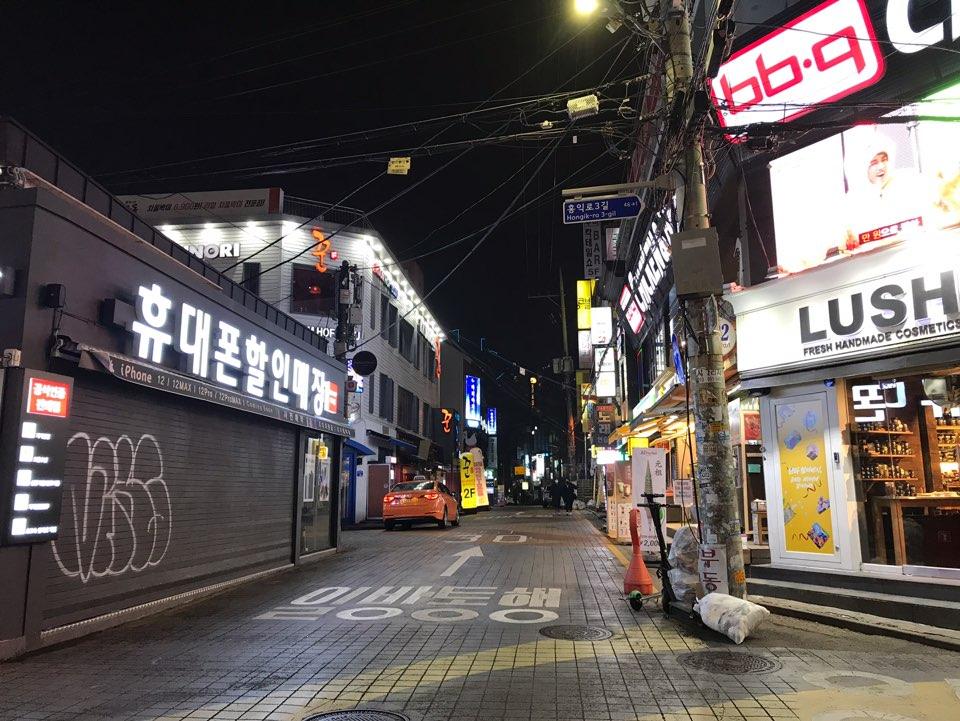 首尔弘大夜晚步行街，闪烁的店铺标志，行人零星。