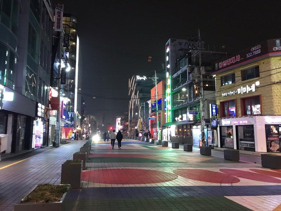 首尔弘大餐饮店与便利店夜晚街景，灯光辉映，街道行人稀少。