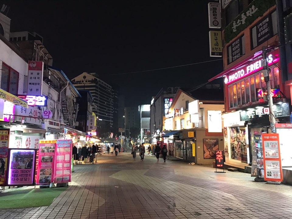 首尔弘大商区商店夜晚景象，店面灯光辉煌，顾客稀少。