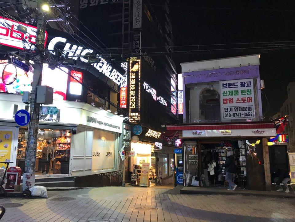 首尔弘大M PlayGround商店夜晚景象，左侧路面空旷，人流稀少。