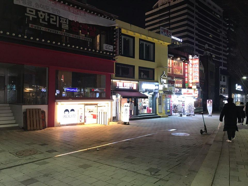 首尔弘大大道沿街夜景，灯光璀璨，行人稀少。