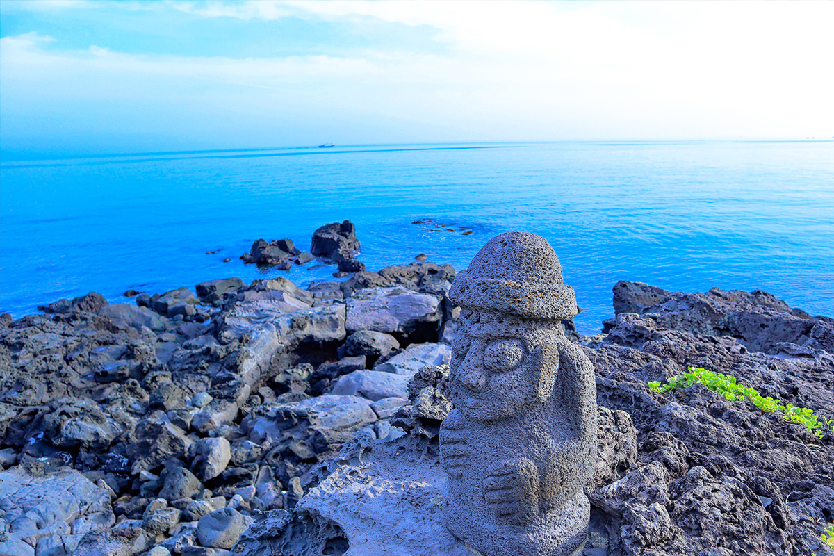 濟州海女正在岩石灘上前行，展示出濟州特有的海女文化和自然環境，女性們身穿潛水服並帶著捕獲工具。
