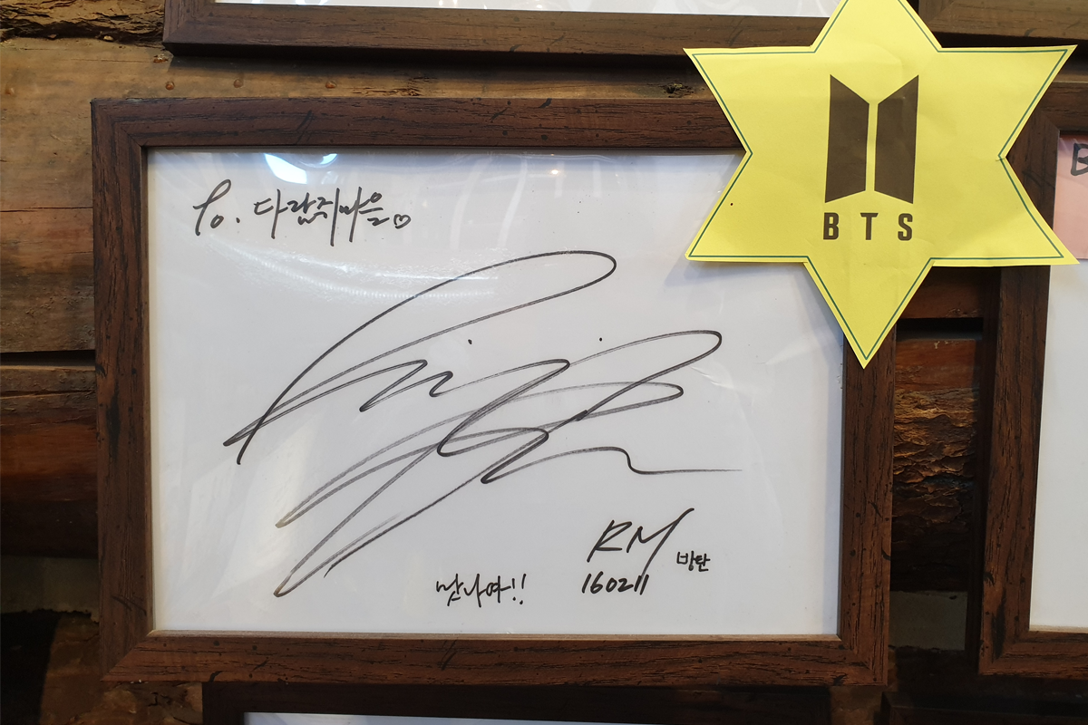 一幅RM簽名在松鼠村鍋巴燉雞餐廳的照片，旁邊貼有BTS標誌