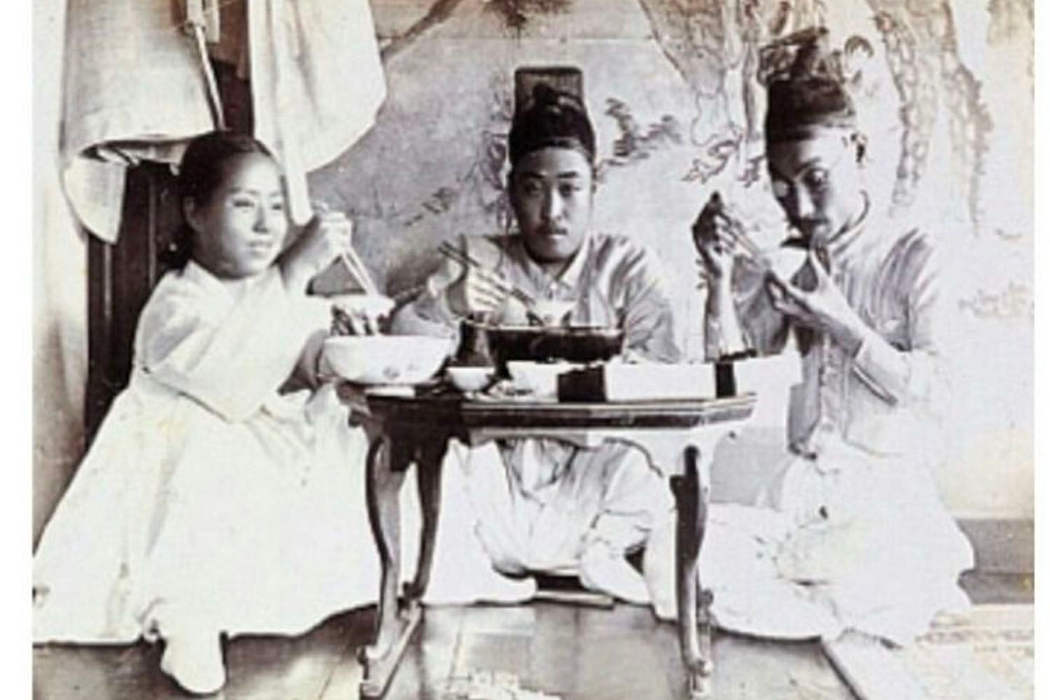 Hình ảnh lịch sử về người mặc trang phục truyền thống Hàn Quốc đang ngồi quanh bàn phẳng thấp với bát cơm trên bàn