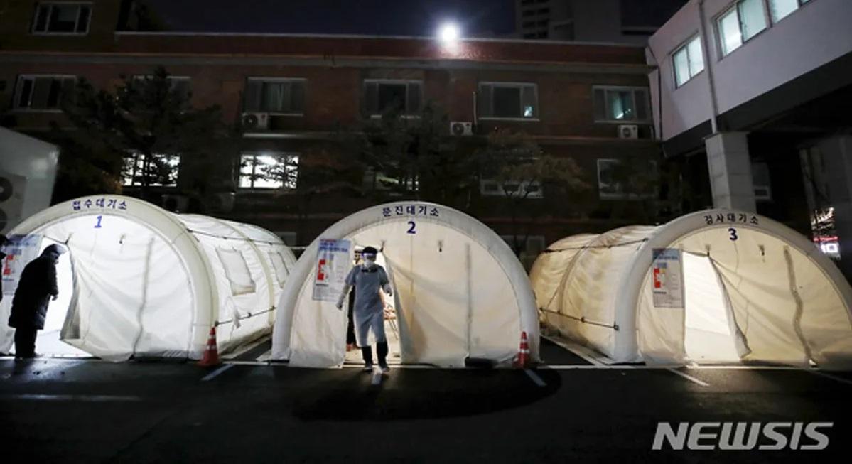 เต็นท์ตรวจหาเชื้อ COVID-19 ที่ตั้งอยู่หน้าสถานพยาบาลในประเทศเกาหลีใต้ โดยมีเจ้าหน้าที่สวมชุดป้องกันเชื้อเดินอยู่