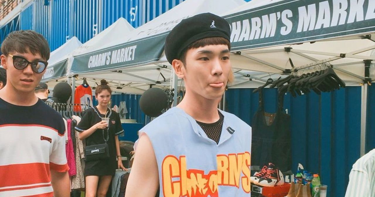 Charm's潮牌市場內部，韓國偶像穿著休閒服飾，背景有店鋪和其他顧客。