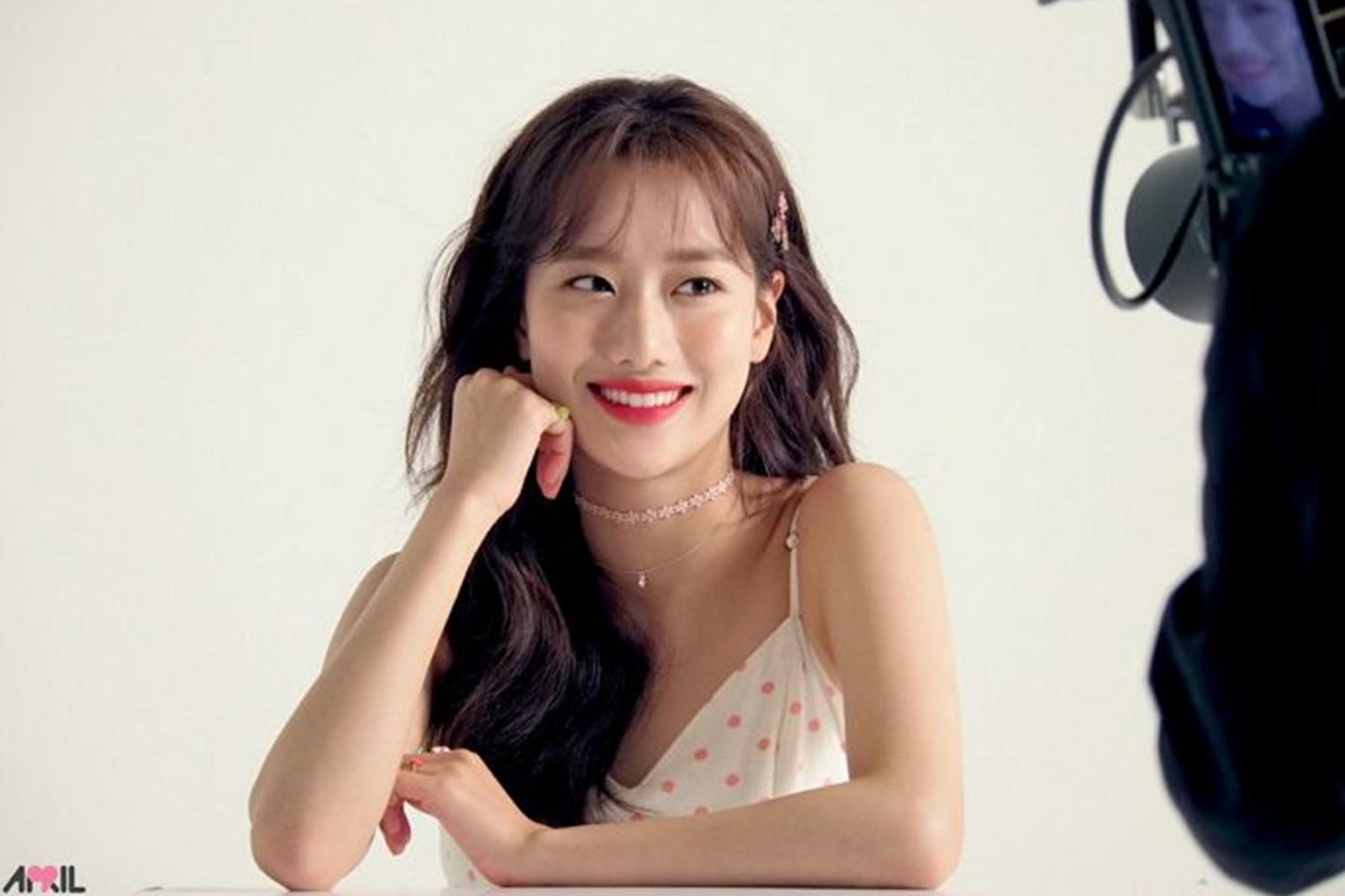 女偶像成員，身穿粉色小點吊帶裙，長髮披肩，甜美地坐在拍攝棚中。