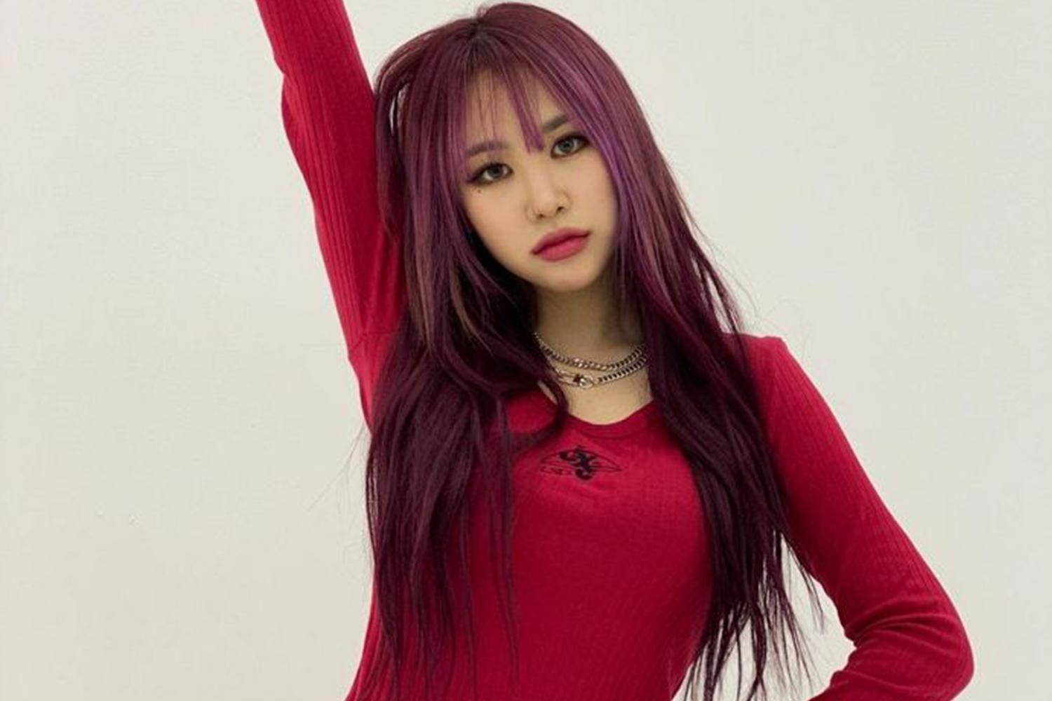 年輕女歌手，身穿紅色長袖上衣，頭髮披肩，看似正在準備表演。