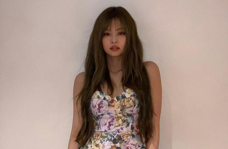 BLACKPINK 成員 Jennie 穿著花卉圖案連衣裙站著，背景為淺色牆壁。