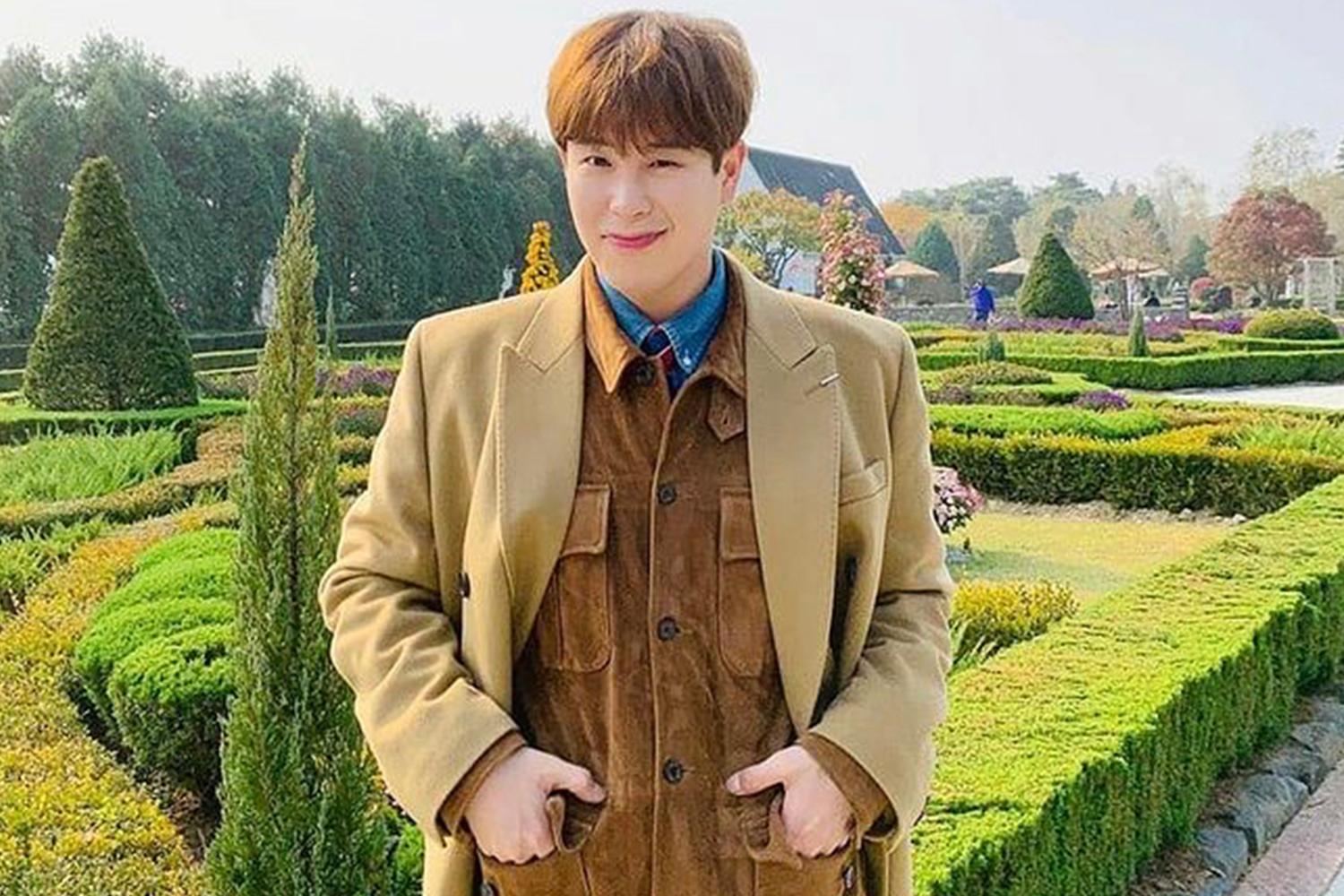 Block B 的成員 P.O 站在一個風景優美的花園裡，穿著米色外套展示休閒時尚。