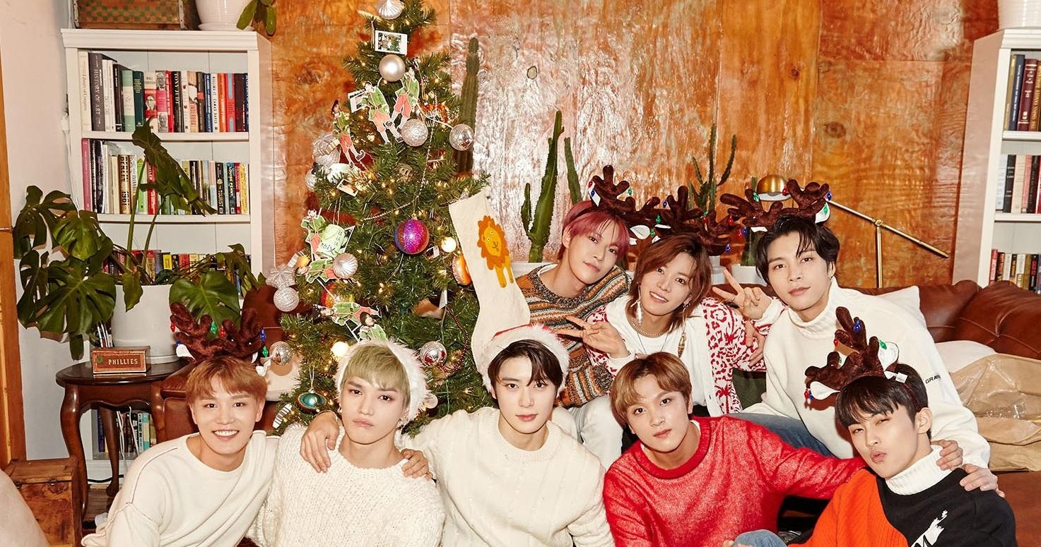 กลุ่มคนแต่งกายชุดวันคริสต์มาสรวมตัวถ่ายรูปหน้าเครื่องต้นคริสต์มาสที่ประดับตกแต่งอย่างสวยงามในบรรยากาศสบาย ๆ