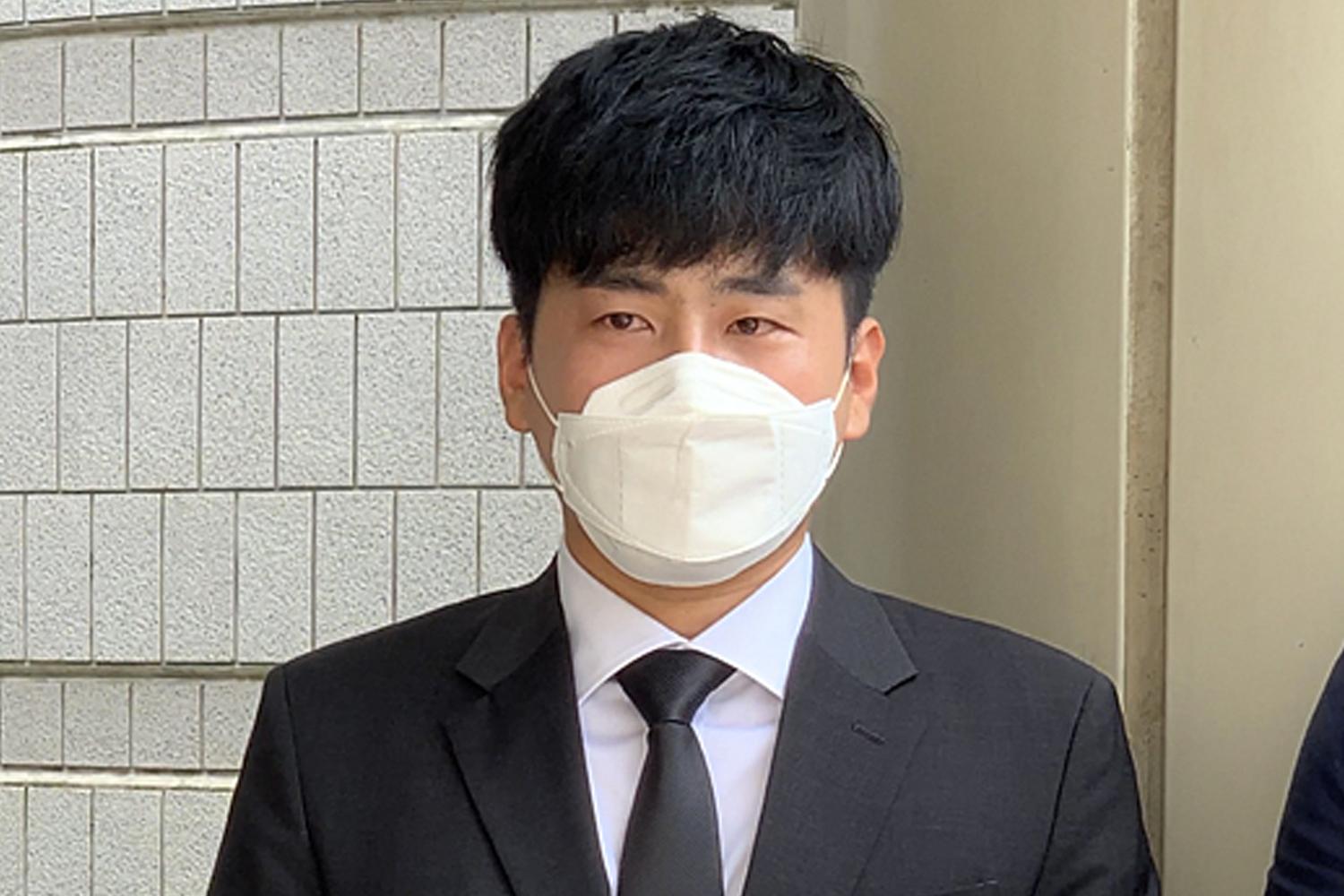 ชายในชุดสูทและเน็คไทสีดำยืนหน้ากำแพงอิฐ