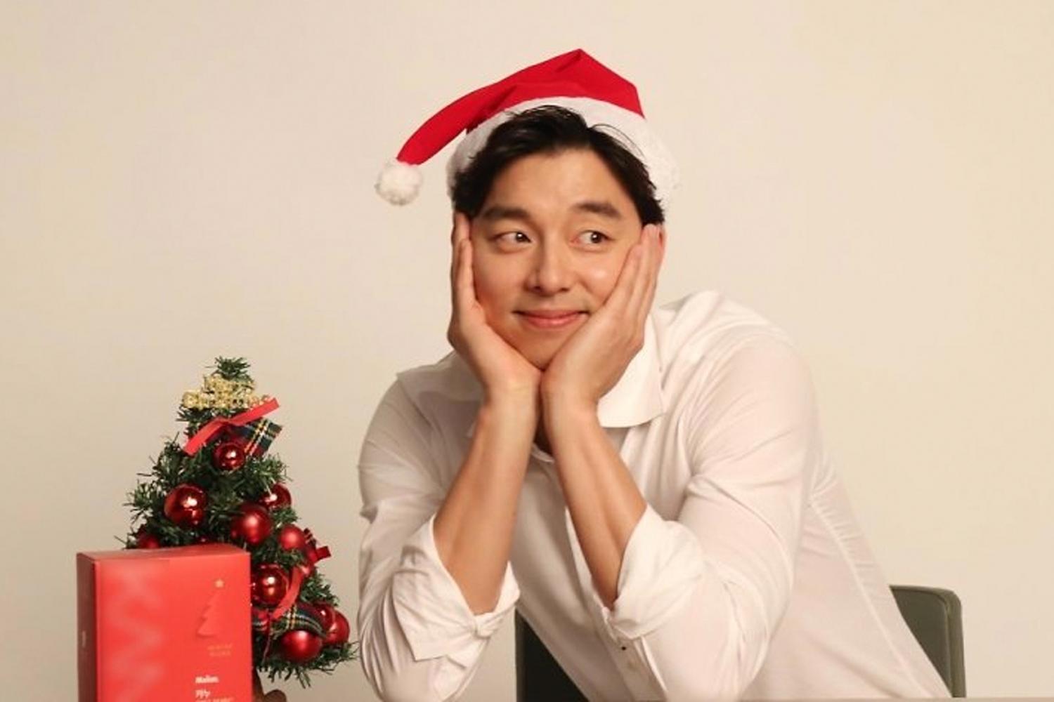 韓國藝人穿著白色襯衫，頭戴聖誕帽，配上小型聖誕樹和禮物盒，傳遞節日的温馨感。