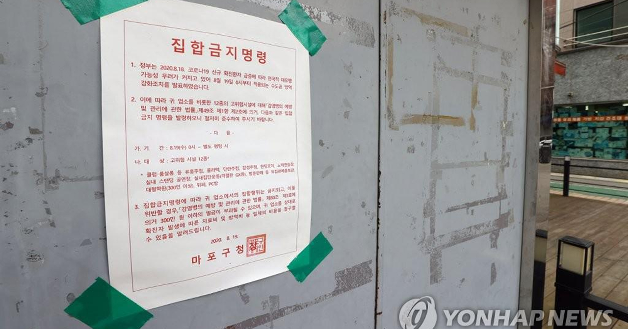 韓國市政貼出的公告，通知居民關於疫情下的集會禁令，呼籲市民遵循規定以防疫擴散，背景為城市的街景。