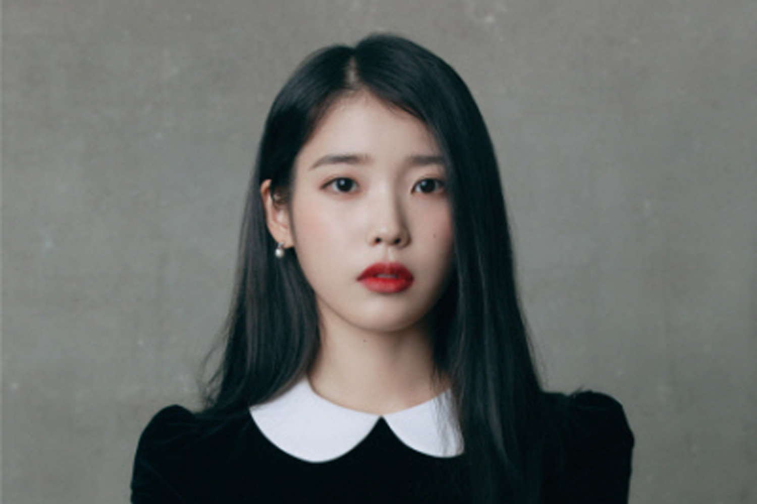 韓國藝人IU的學生時代，身著黑色衣服，背景為灰色牆壁，展現出她年輕時的模樣。