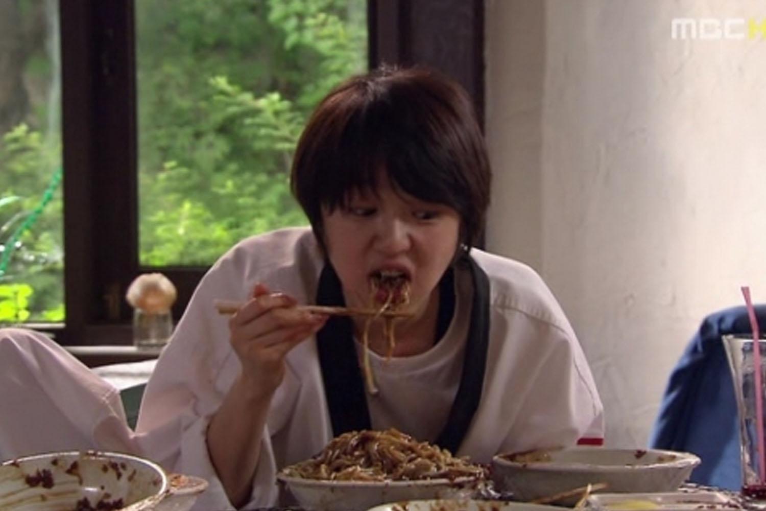 ชามบะหมี่จาจังมยอน สีดำเค็มหวาน บนโต๊ะที่มีถ้วยอาหารเกาหลีอื่นๆอยู่ด้วยจากฉากในซีรีส์เกาหลี