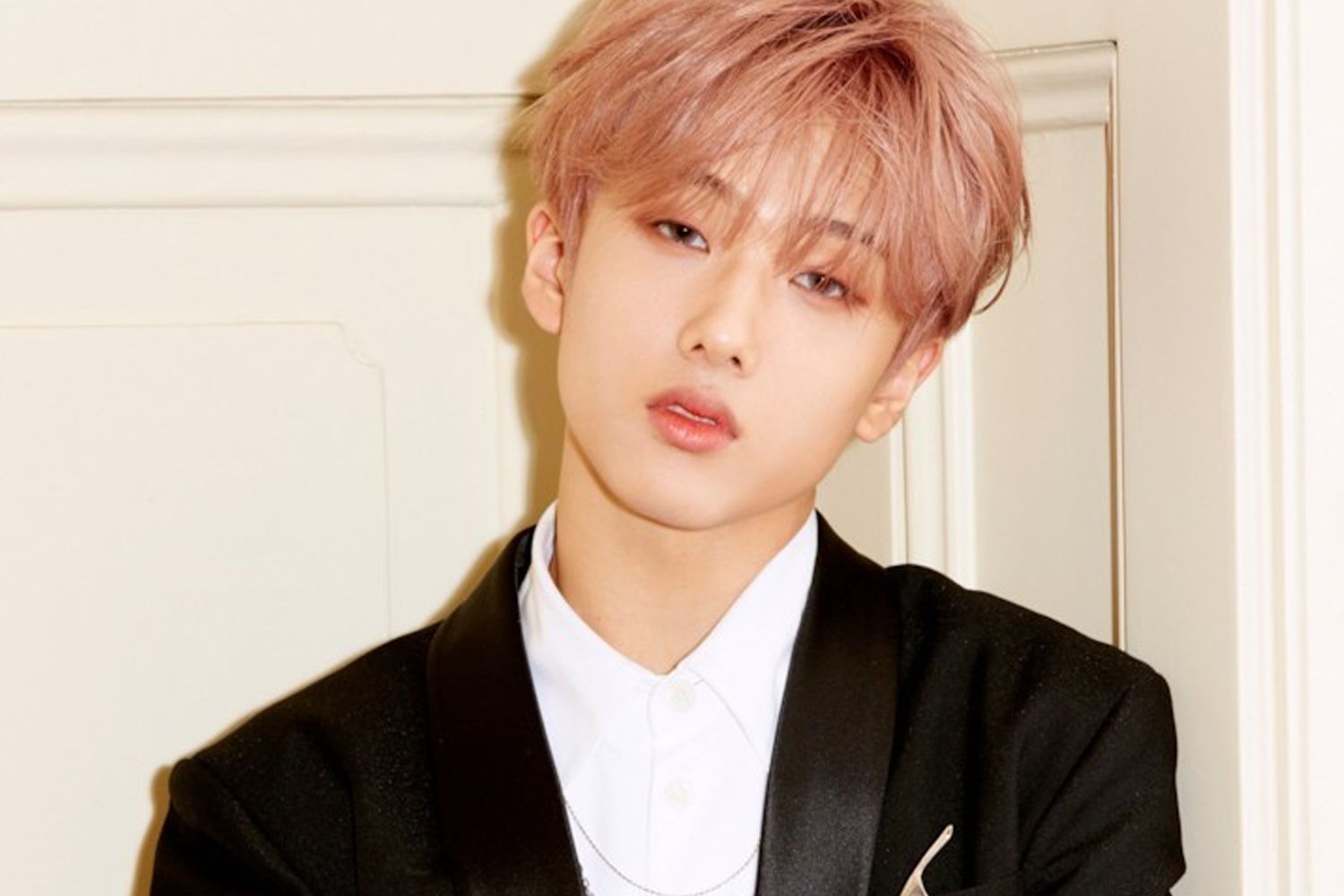 韓國男子組合NCT的成員志晟，站在白色背景前，穿著黑色西裝，展露出時尚氣質