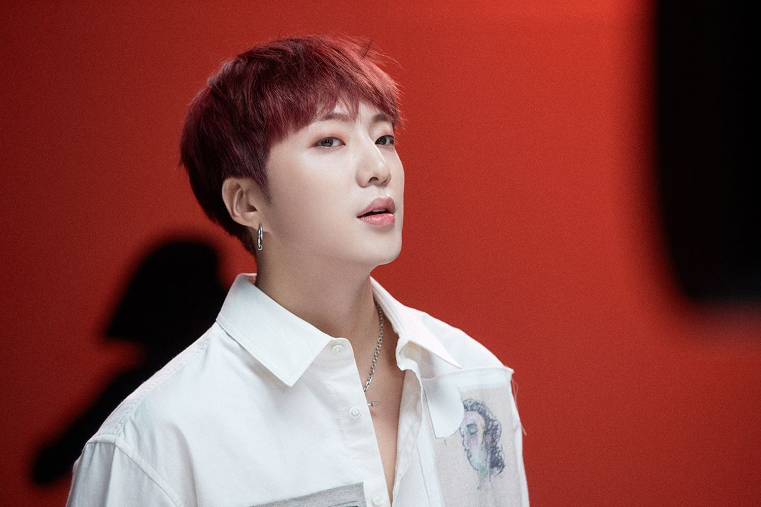 韓國男子組合WINNER的成員昇潤，穿著白色襯衫站在紅色背景前，展現時尚風格