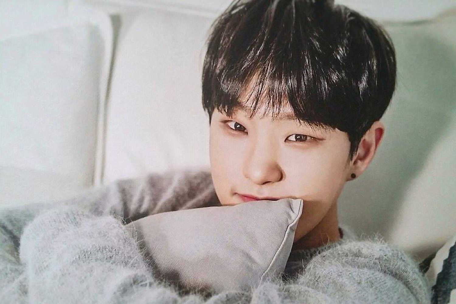 韓國男子組合Seventeen的成員Hoshi，穿著灰色毛衣，坐在白色沙發上，顯得温暖而舒適