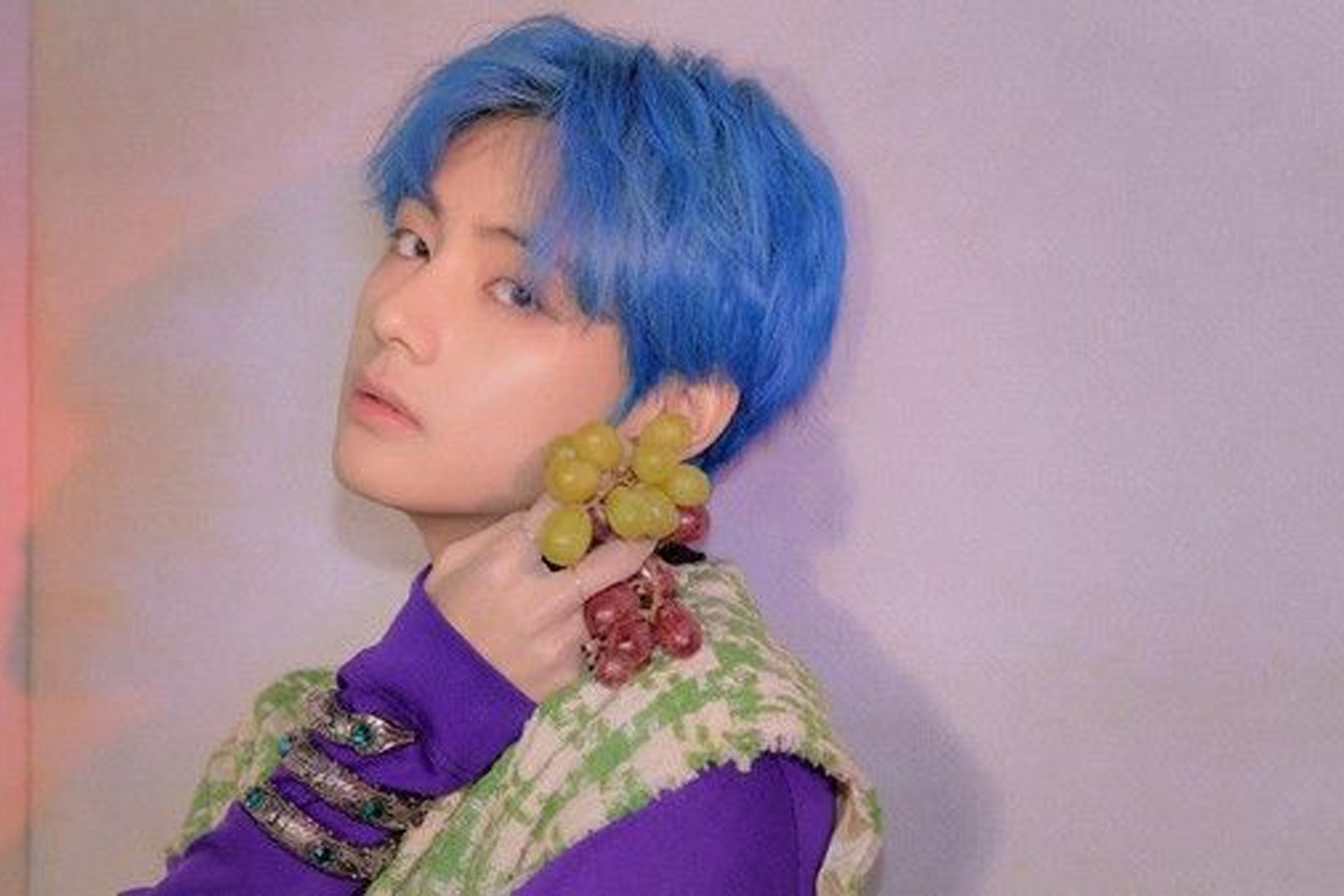 韓國男子組合BTS的成員V，身穿紫色服裝，拿著葡萄，展現獨特個人風格