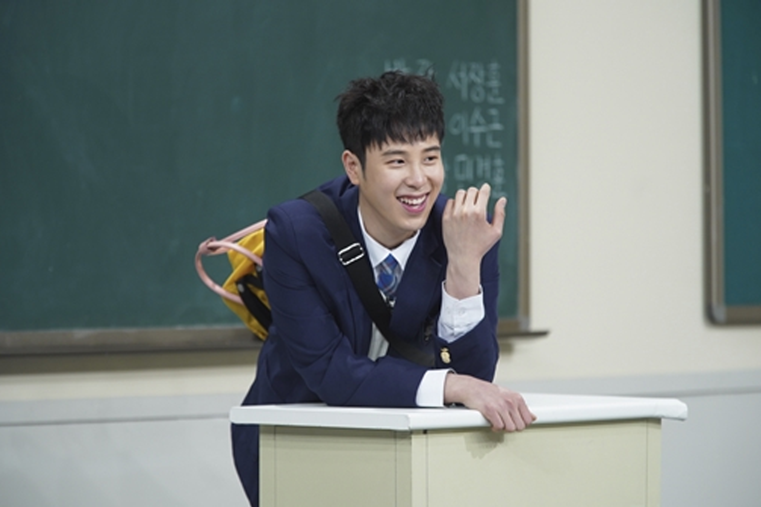 韓國男子組合Block B的成員P.O，身穿藍色西裝，作出可愛的手勢，背景是一塊綠色黑板