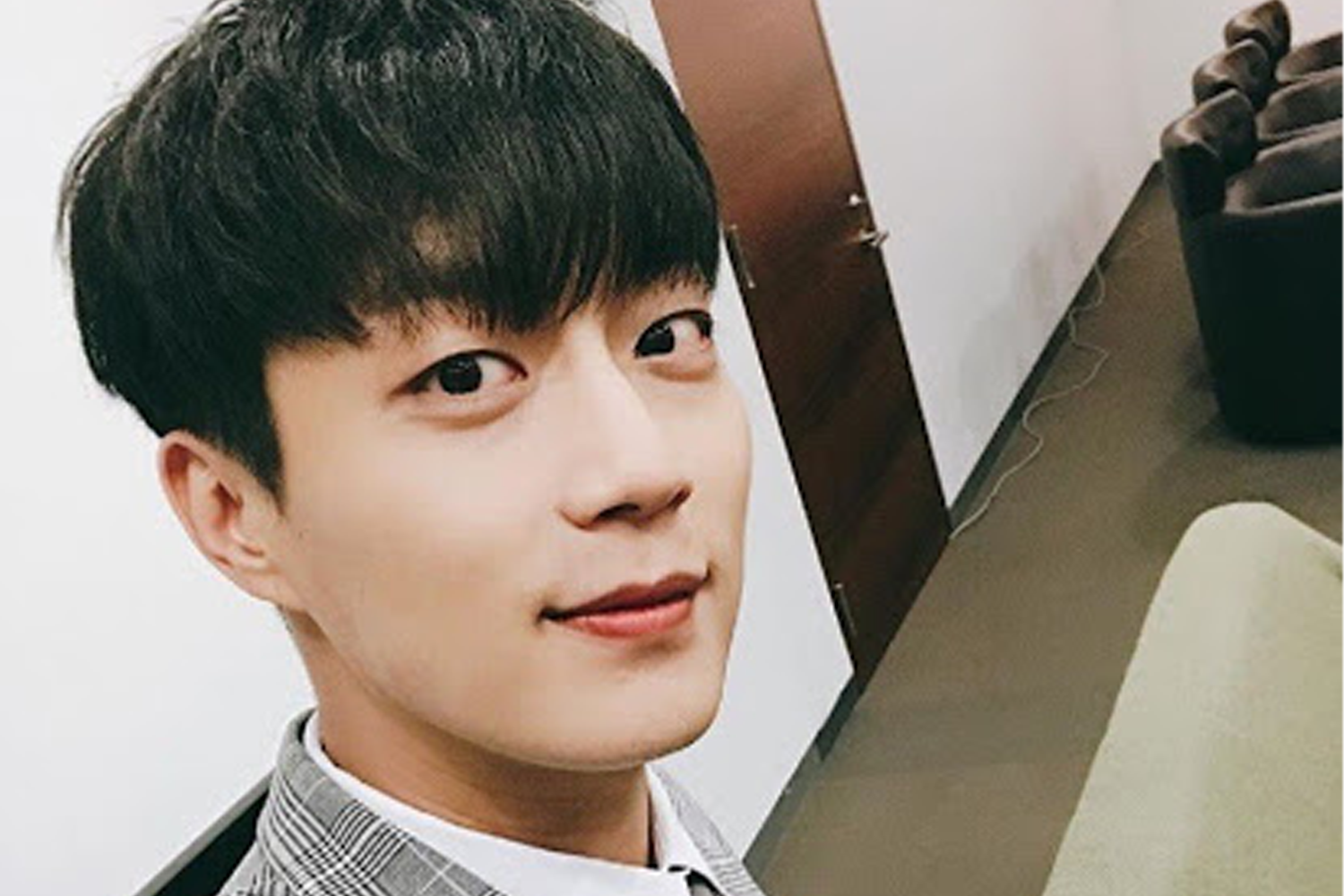 韓國男子組合Highlight的成員鬥俊，穿著灰色格子西裝，站在休息室內，散發成熟魅力