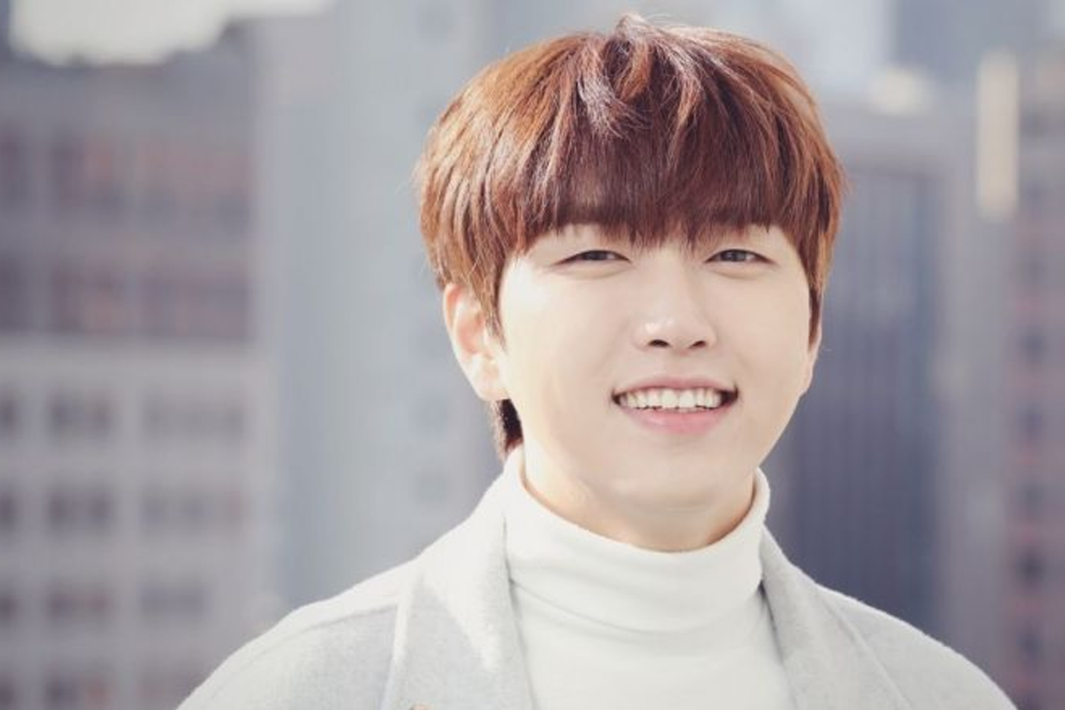 韓國男子組合B1A4的成員燦多，身穿白色高領針織毛衣，立於城市背景下，微風拂面，顯得陽光而自信