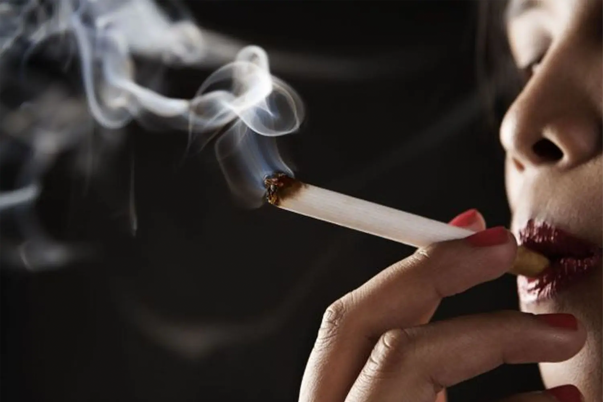 手持香煙正在吸煙，煙霧環繞在黑色背景中。