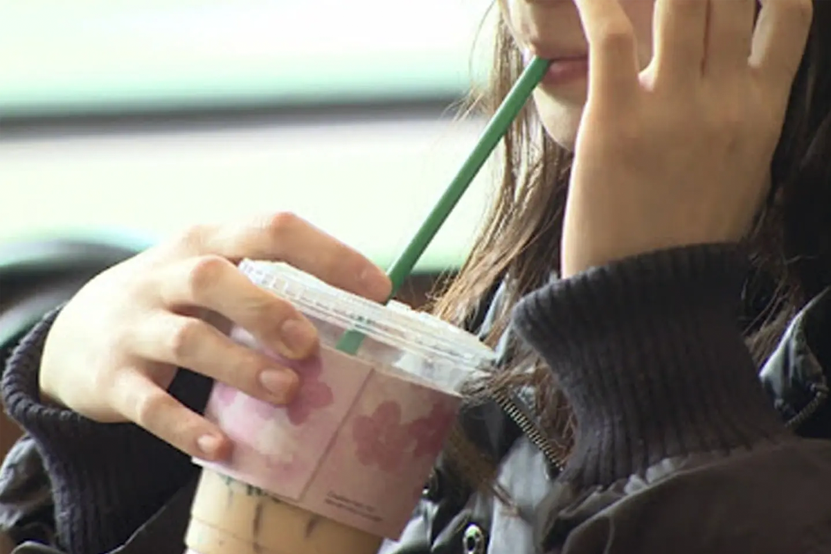 一名女性手持杯子正在用吸管喝咖啡，顯示飲料的顏色可能會影響牙齒顏色。