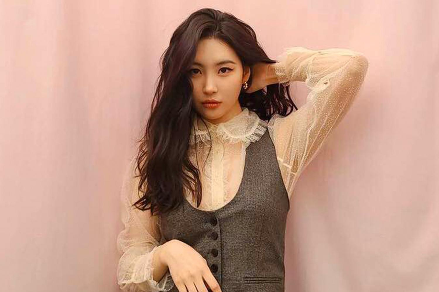 宣美站在粉紅色背景前，穿著白襯衫和深色外套，以戲劇性的姿勢擺姿勢。