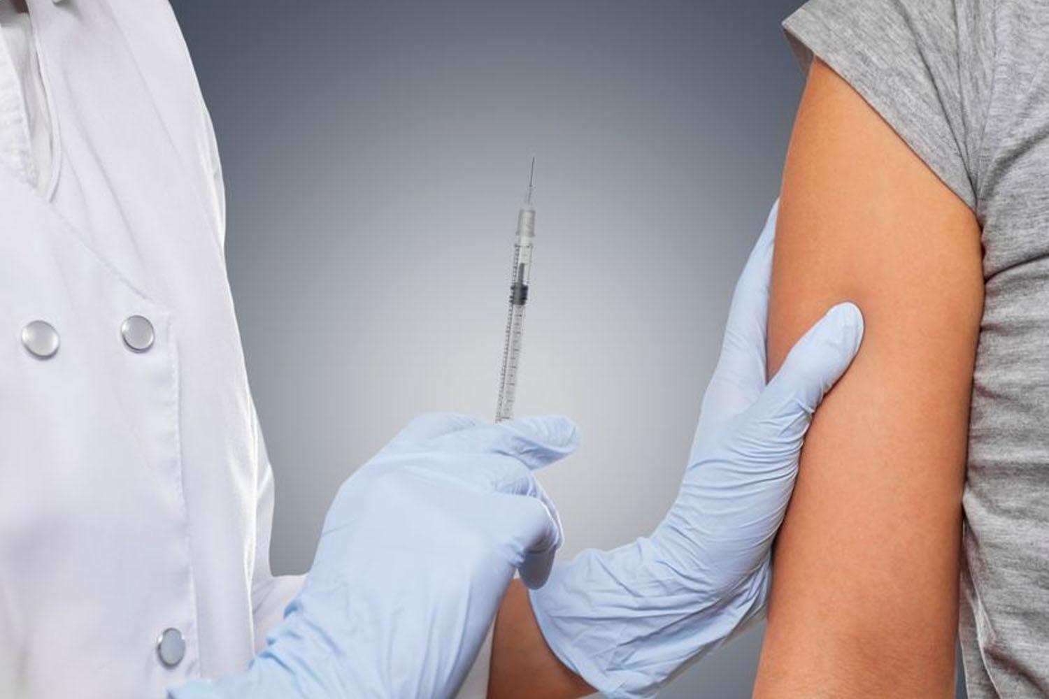 แพทย์กำลังฉีดวัคซีนให้กับผู้ป่วยในชุดสีขาว ขณะสวมถุงมือสีฟ้า ถือเข็มฉีดยาเพื่อเตรียมฉีดวัคซีนเข้าที่แขนซ้ายของผู้ป่วยคนหนึ่ง ภาพนี้แสดงถึงกระบวนการการฉีดวัคซีนในเกาหลี ซึ่งรวมถึงมาตรการที่สำคัญในช่วงการระบาดของโควิด-19 ประโยคสำคัญ: การเตรียมวัคซีนและการฉีดวัคซีนเป็นขั้นตอนในการจัดการกับโรคระบาด อย่างไรก็ตามข้อมูลเกี่ยวกับการแจกจ่ายวัคซีนยังคงเป็นเรื่องที่น่าติดตามในเกาหลี ณ ขณะนี้ 