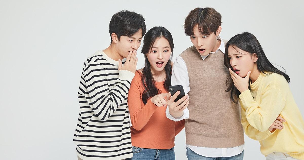 กลุ่มของคนหนุ่มสาวกำลังมองที่โทรศัพท์มือถือด้วยความสนใจ ภาพนี้ใช้อธิบายถึงแอปพลิเคชันที่นิยมใช้ในเกาหลี.