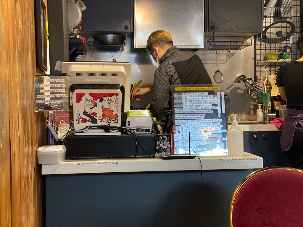 Drunken Vegan рестораныг харуулсан, гал тогооны хэсгийн доторх өхөөрдөм зурвасуудтай дүр зураг. Онцлох зүйлсийг зэрэгцээ тавьсан нь харагдаж байна.