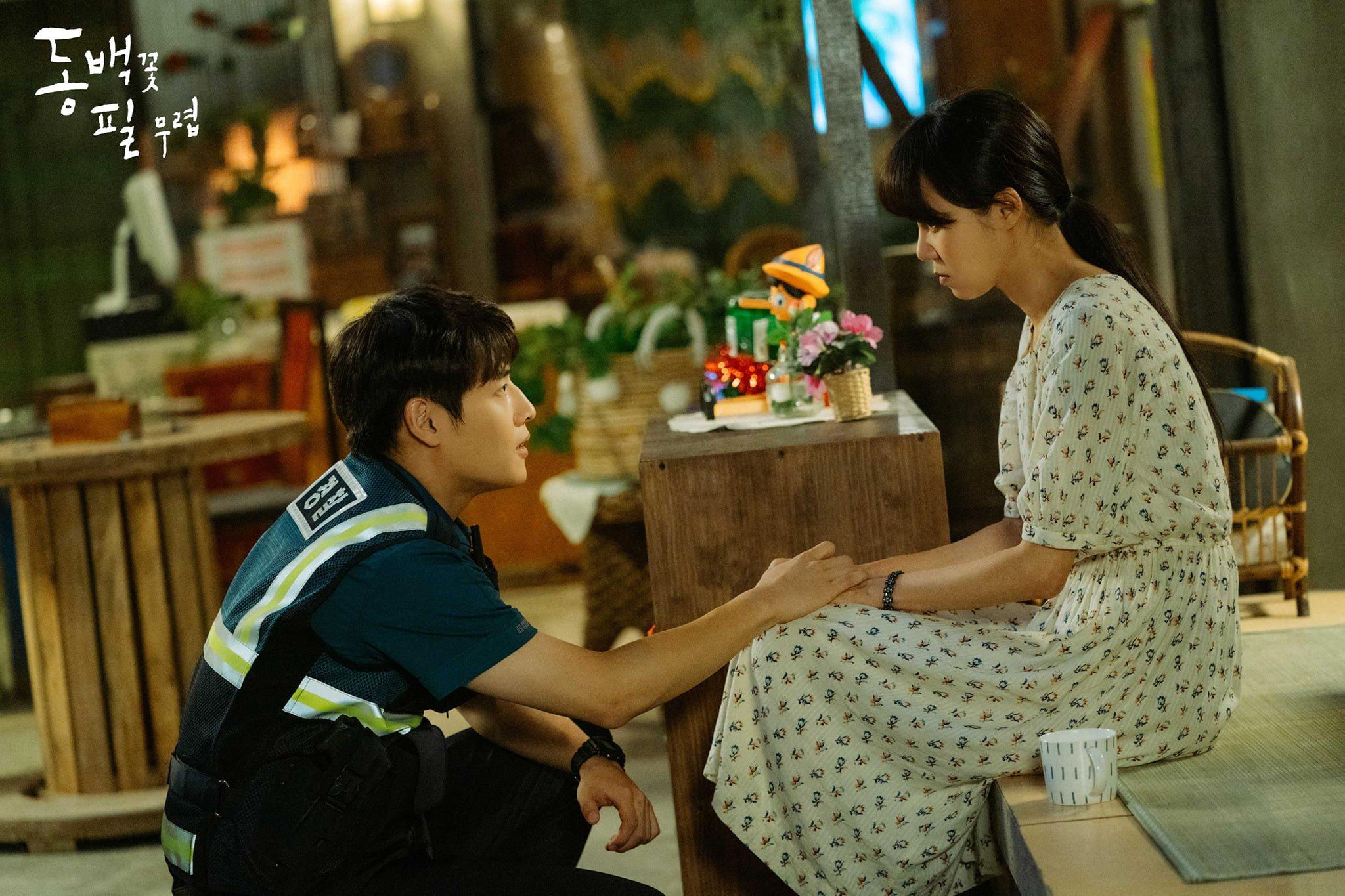 ฉากจากซีรีส์เกาหลีที่ตัวละครตำรวจนั่งพูดคุยกับหญิงสาวสวมชุดเดรสลายดอกในบรรยากาศอบอุ่น