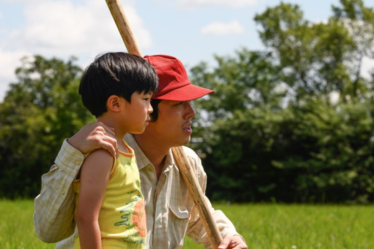 電影《夢想之地》中的一個溫馨瞬間，父親抱著兒子，背景是一片綠色的田野。