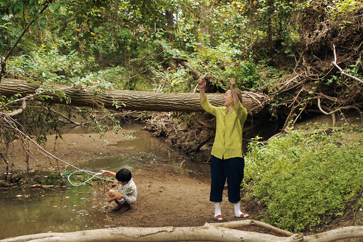 《夢想之地》中在小溪旁玩耍的孩童，旁邊站著身著黃色襯衫的角色。