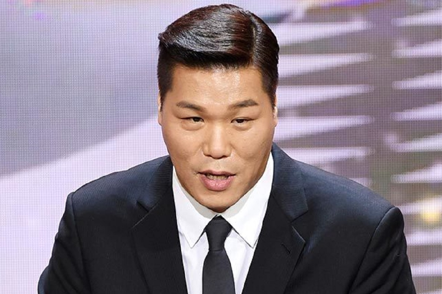 韓國MC姜虎東身著正裝，參與綜藝活動的專業形象。