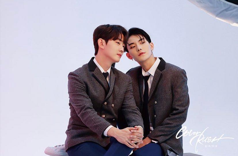 นักเรียนชายสองคนในชุดนักเรียน โดยคนหนึ่งนั่งบนเก้าอี้และอีกคนพิงที่ไหล่ ดูอบอุ่นและใกล้ชิดในสภาพแวดล้อมที่เป็นทางการ