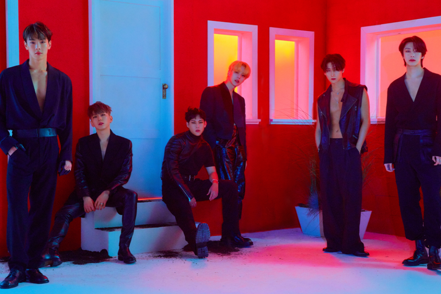 六名男團偶像成員，身穿黑色衣服，站立在紅色背景前，色彩深沉且畫面充滿時尚感。