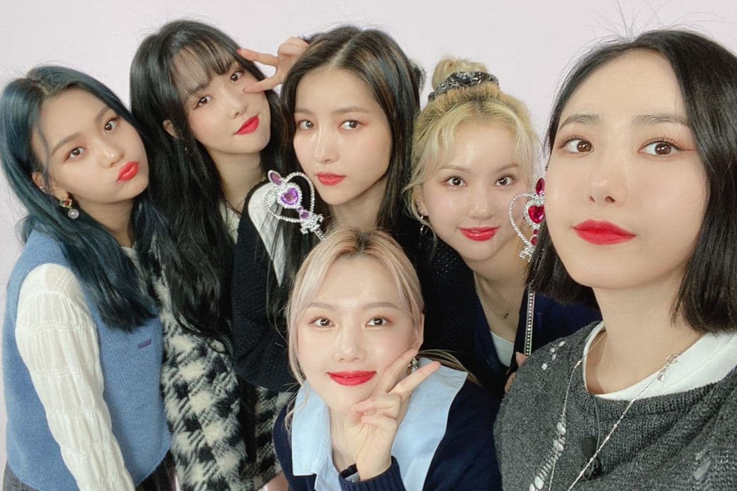 一羣女團成員聚集在一起，靠得很近，互相笑著，身穿不同顏色及樣式的服裝，展現友好關係。