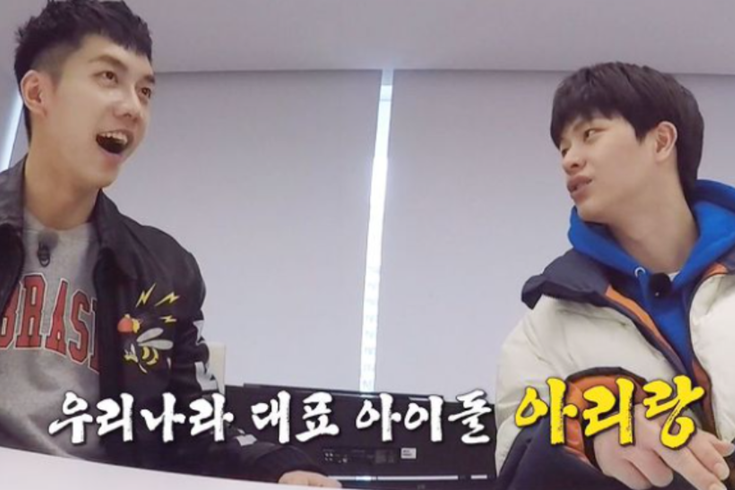 兩位男性偶像在室內穿著休閒服裝，進行交流，背景窗户透著白光，對話呈現輕快氣氛，以白色字體顯示他們的討論內容。