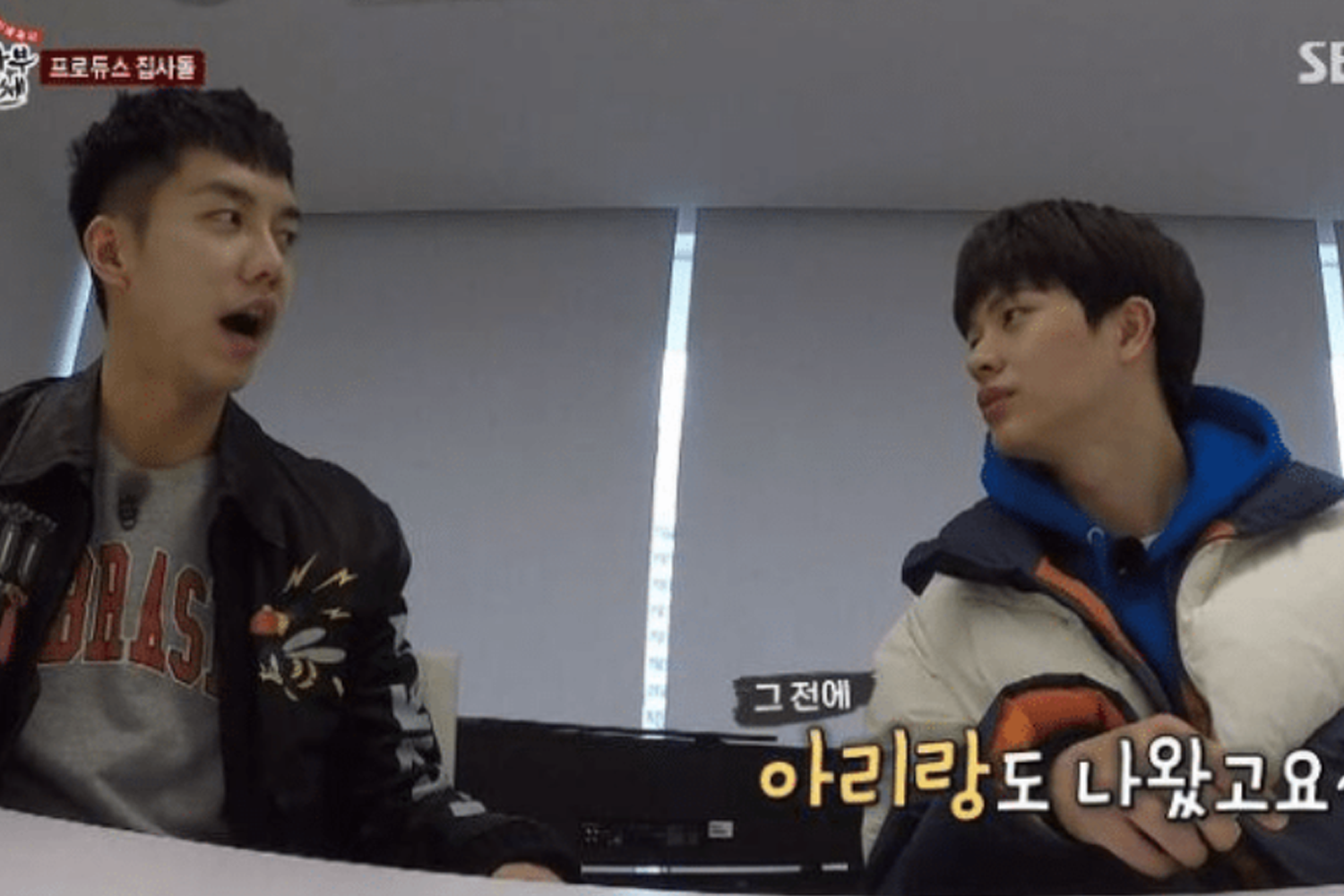 兩位男性偶像在室內，穿著休閒服裝，進行輕鬆對話，背景是透光的窗户，整體呈現放鬆的洽談氛圍。