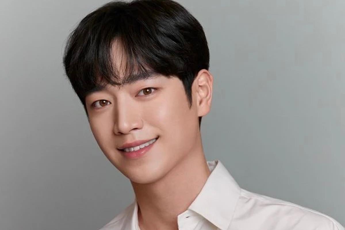 韓國演員徐康俊穿著藍色條紋T恤，站在白色牆壁前，神情專注。