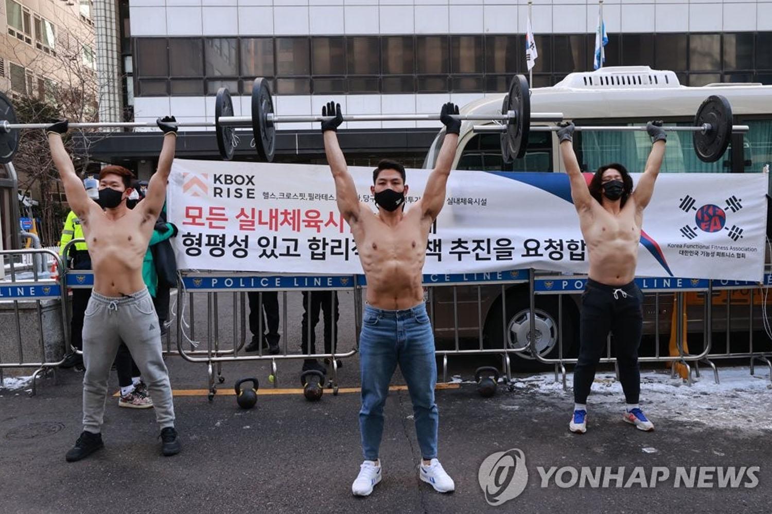 ภาพการประท้วงของผู้ชายที่กำลังยกบาร์เบลล์หน้าสถานที่ราชการเพื่อเรียกร้องเงินชดเชยในการประกอบธุรกิจ