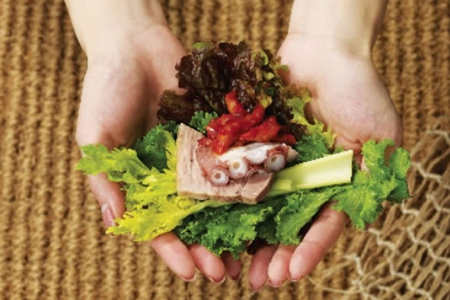 丰富的韩国生菜包饭，手捧新鲜的生菜，内包肉块、泡菜和八爪章鱼，展示韩国美食的独特搭配与风味。