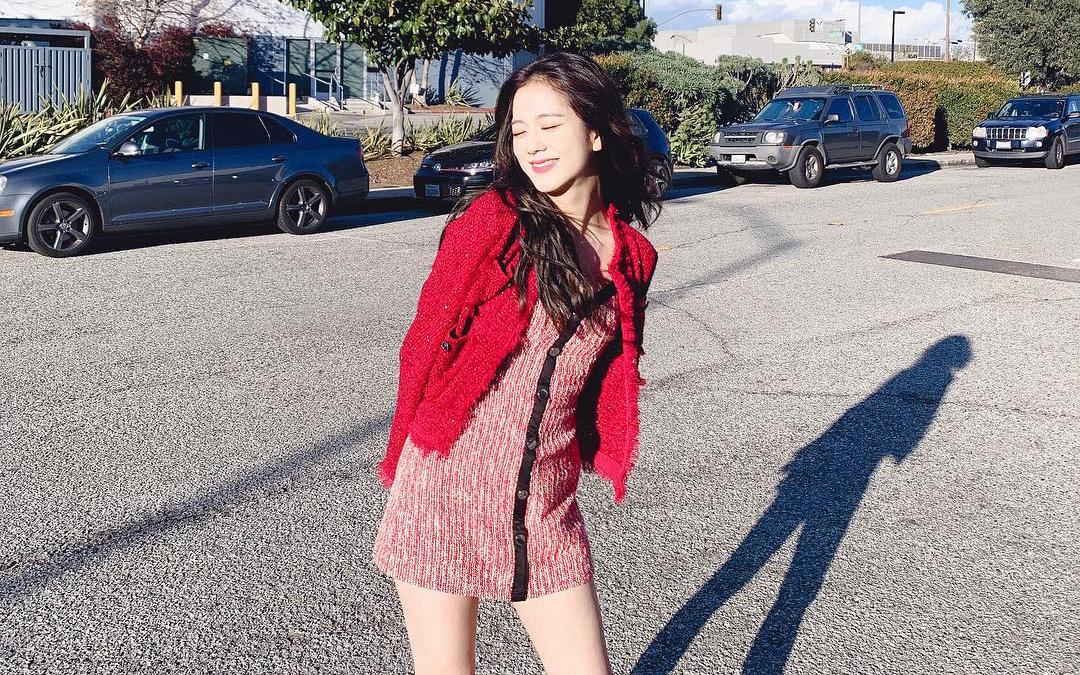 ผู้หญิงสวมเสื้อแจ็คเก็ตสีแดงยืนอยู่กลางถนน มีเงาเกิดขึ้นบนพื้น แสดงถึงสไตล์แฟชั่นและความมั่นใจ