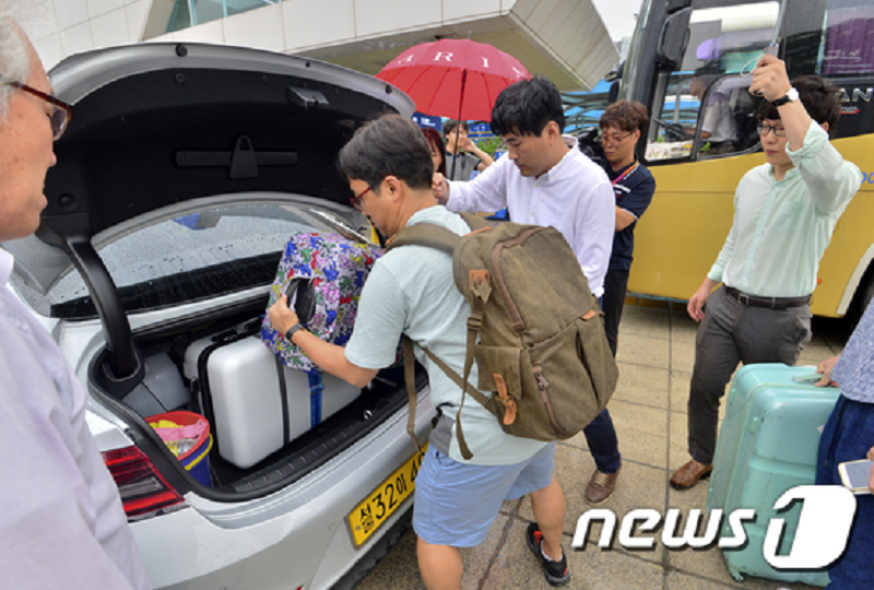韓国で荷物を車のトランクに入れる旅行者のイメージ。空港でのタクシー利用シーンを示し、バックパックとスーツケースを持つ人々が見える。交通と旅行の詳細を提供。